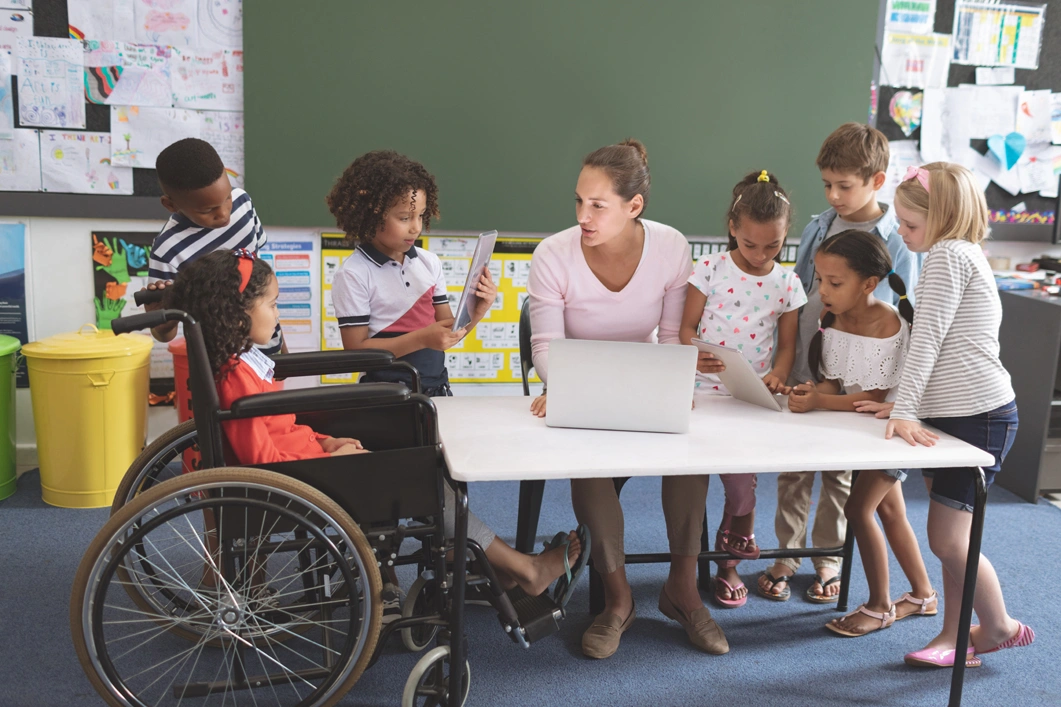 Students using digital tablet while teacher interacting with students in classroom at school