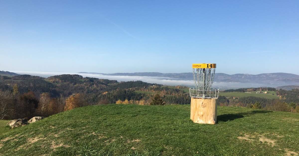 A yellow-banded disc golf basket on a hilltop with mist-covered hills in the distance
