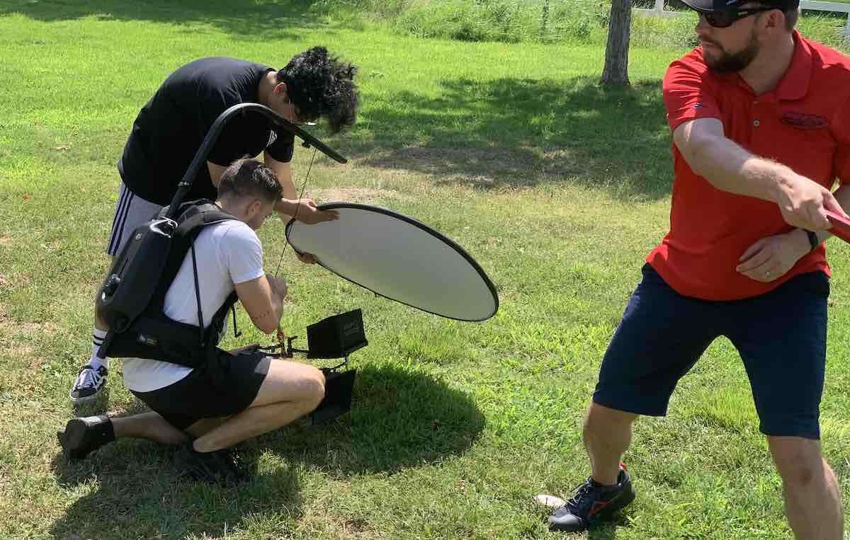 Men with camera equipment filming another man holding a disc golf throwing pose