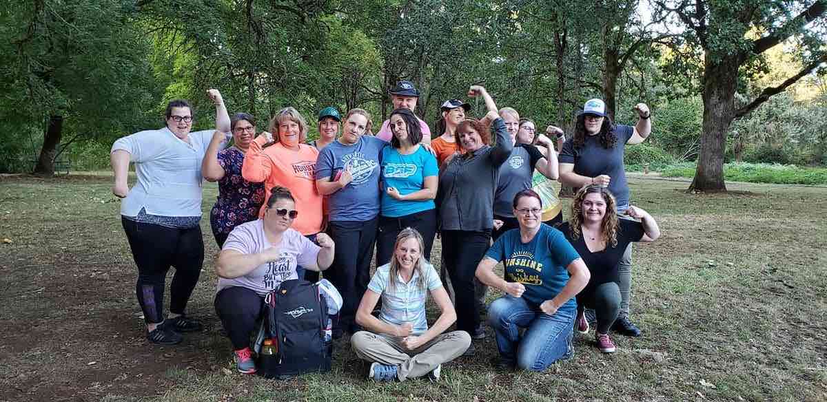 A group of women disc golfers pose for the camera, playfully flexing their arms