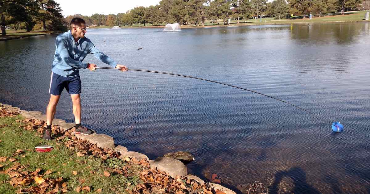 A disc golfer getting a disc out of water with a long, telescopic pole