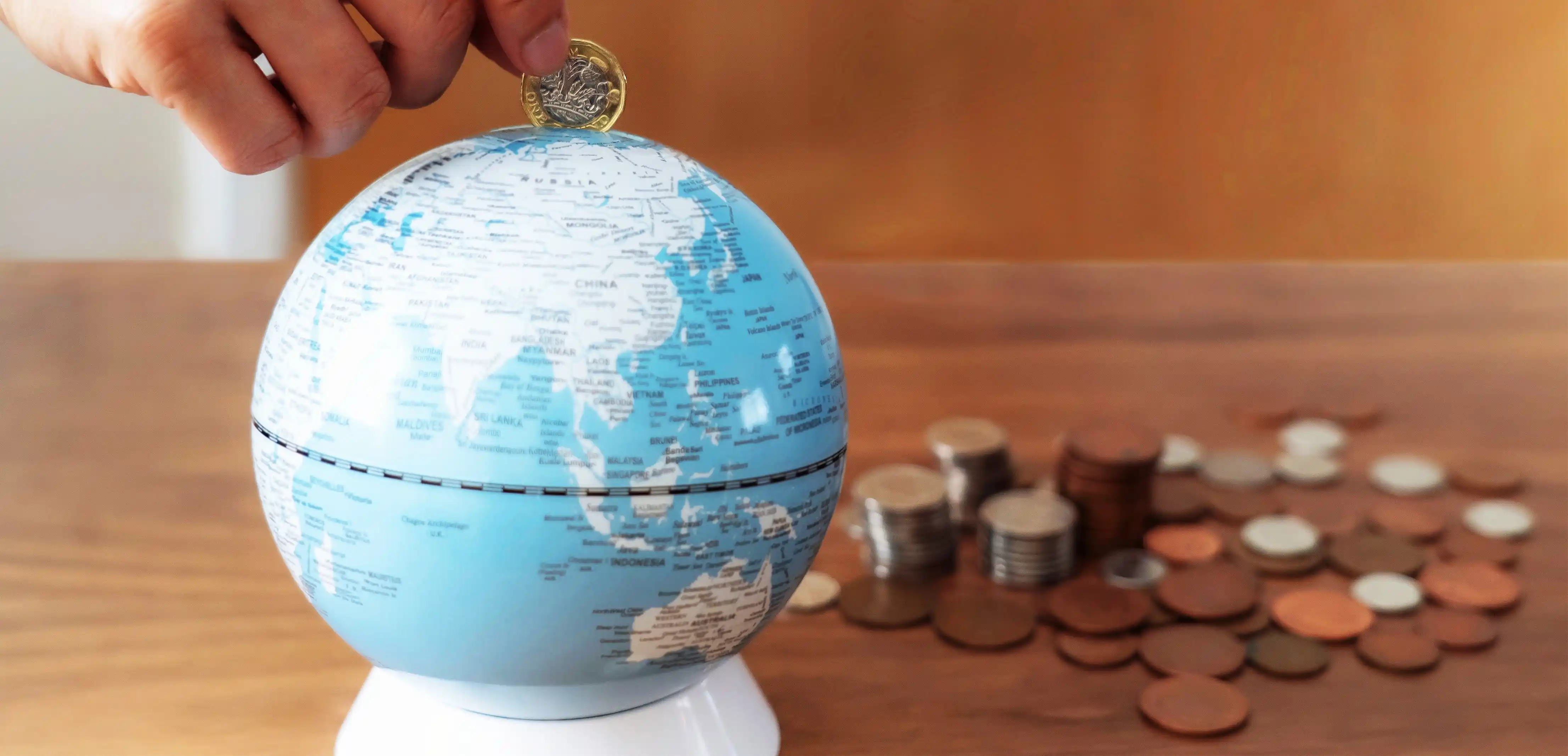 Hand inserting coin into globe piggy bank symbolizing global CSR investment