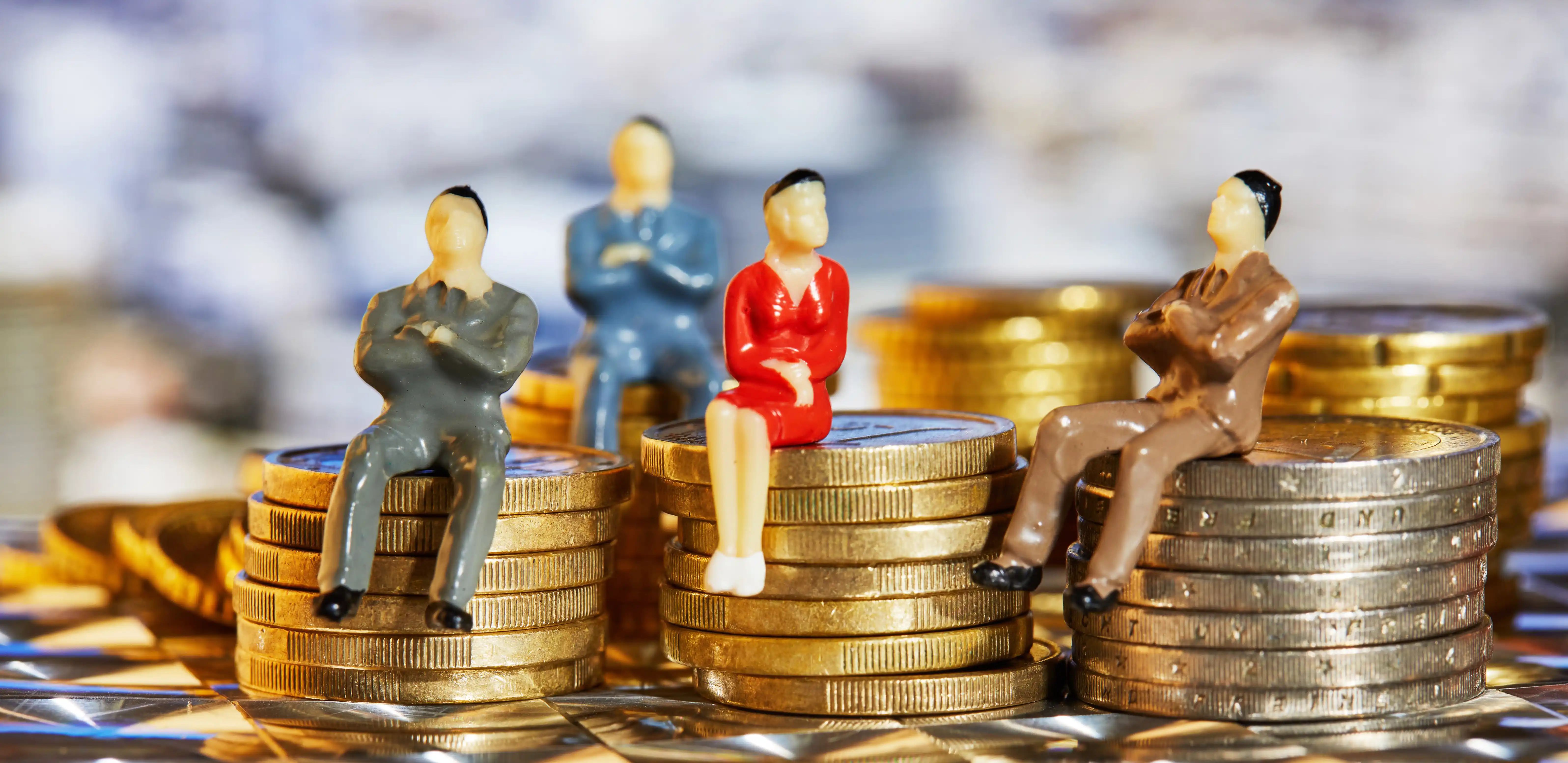 Miniature business figures sitting on stacked gold coins representing fair remuneration and talent retention strategy