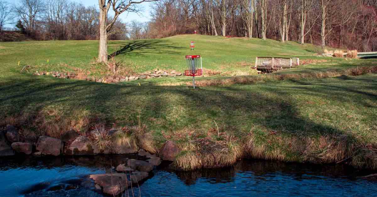 Red disc golf baskets in a field with running water in the foreground