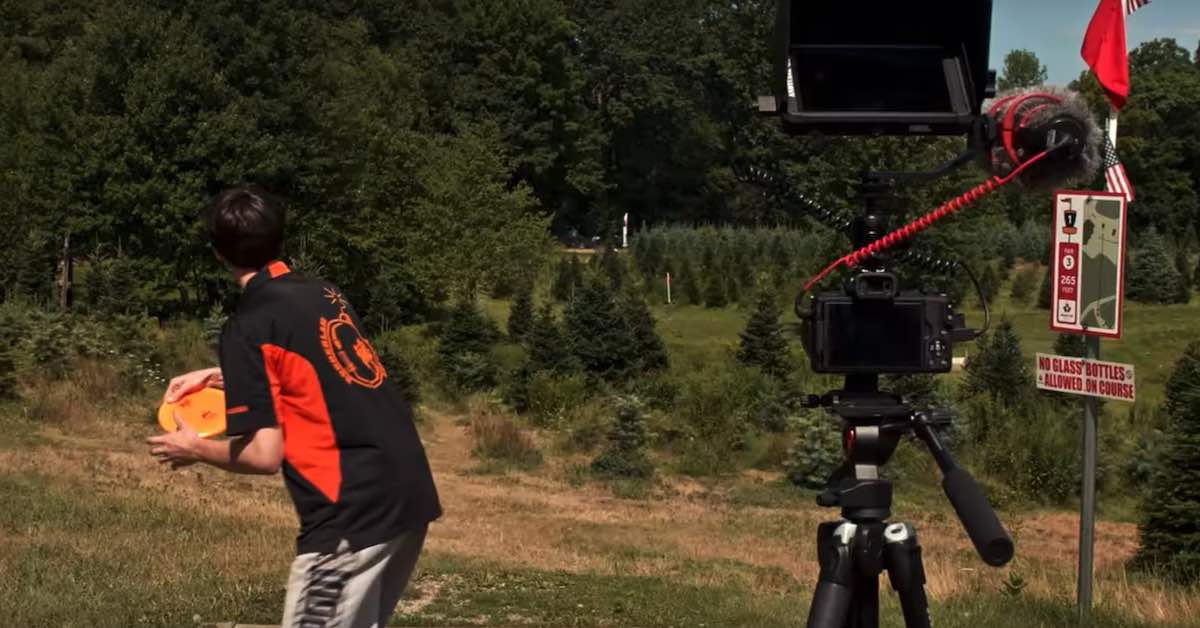 A camera set up filming a player on a disc golf tee
