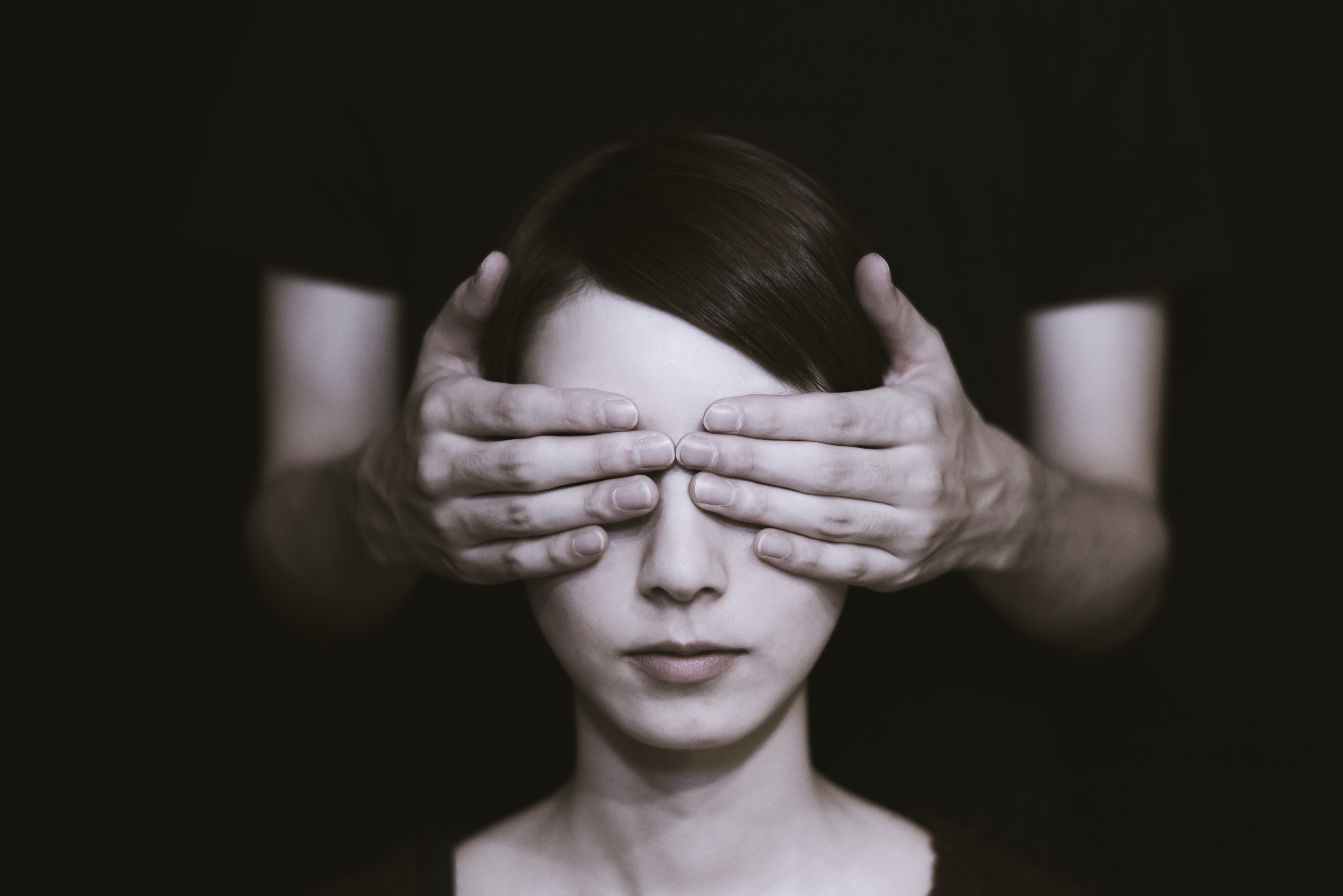 black and white photo of a woman whose eyes are being covering by someone's hands standing behind her