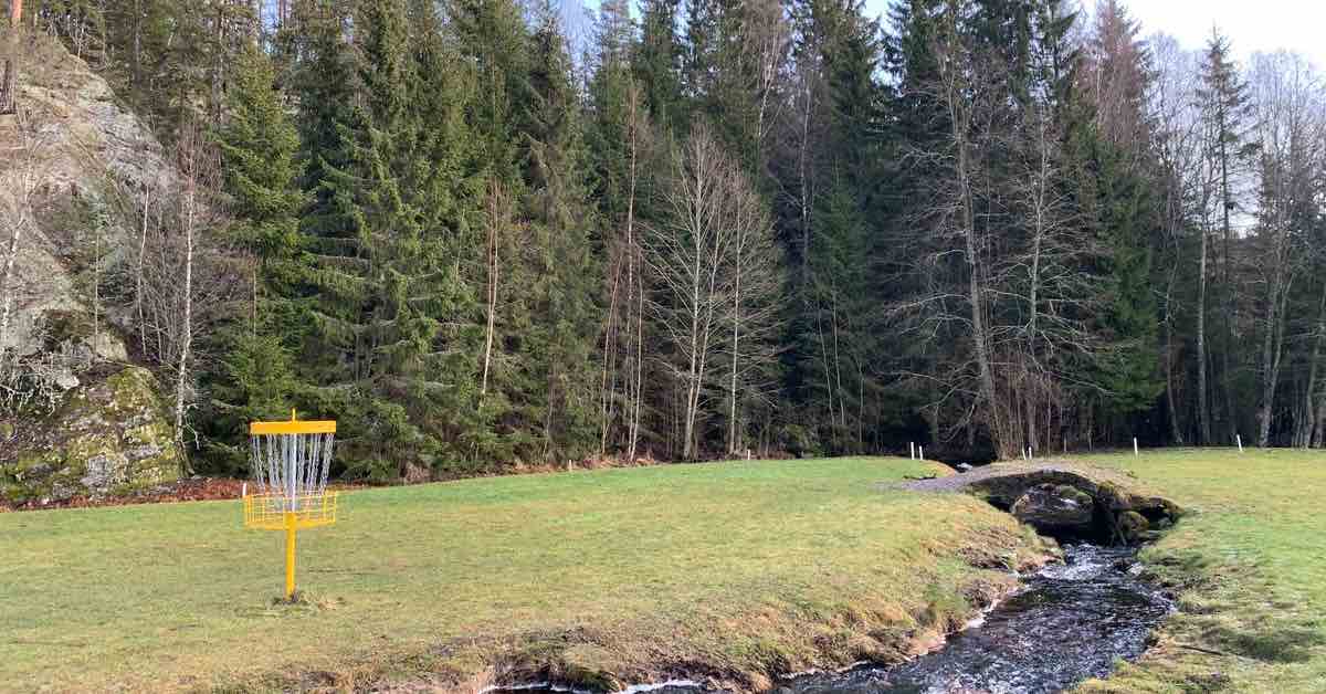 A yellow disc golf basket next to a narrow but quickly flowing stream