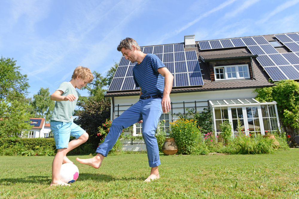 son and father playing in front of solar panel house