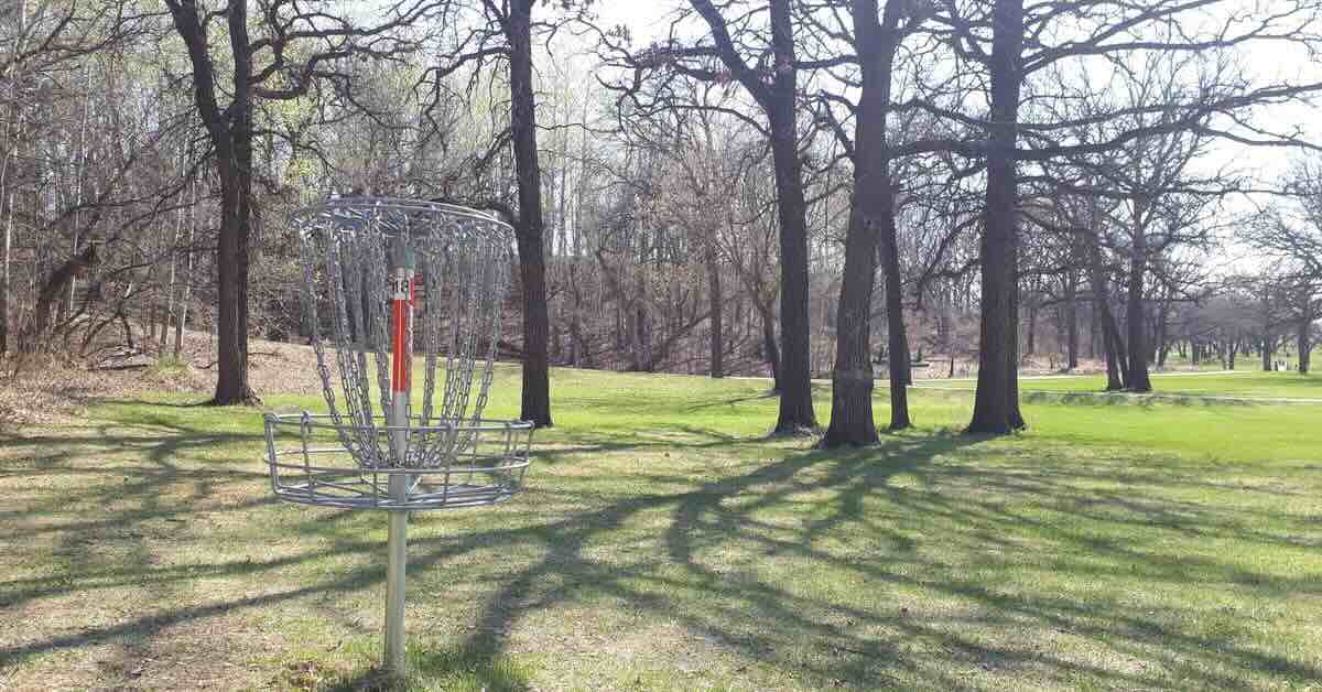 Disc golf basket in a mowed area with scattered trees