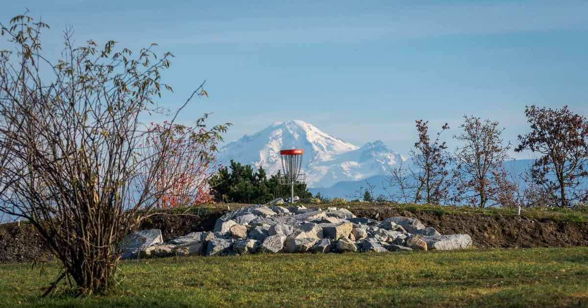 A red-banded disc golf basket on rocks with a snow-covered mountain peak in the distance
