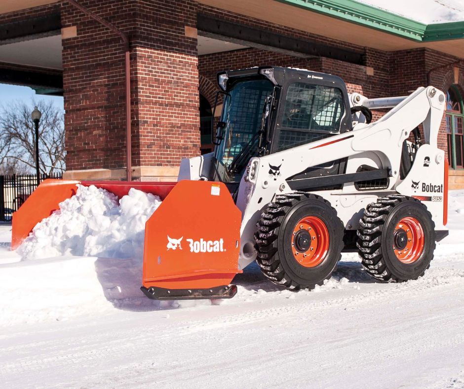 Bobcat skid steer with a snow pusher attachment surrounded by snow