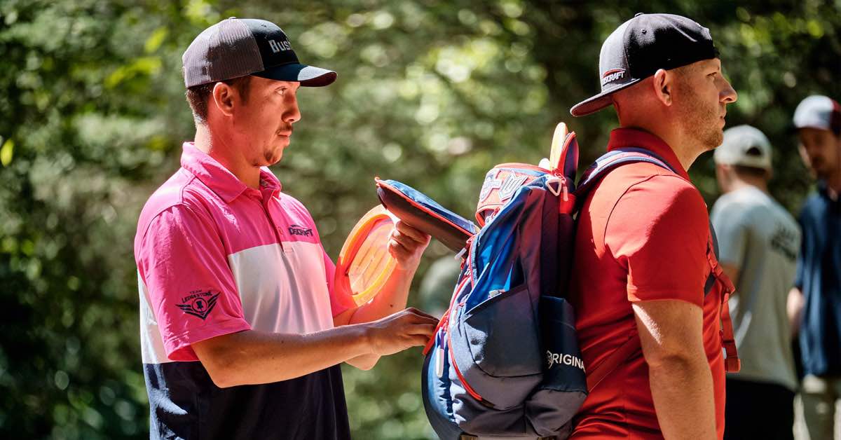 A disc golfer pulls a disc out his bag carried by a caddie