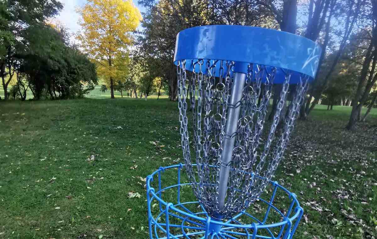 A blue disc golf basket in a park-like setting with thin trees