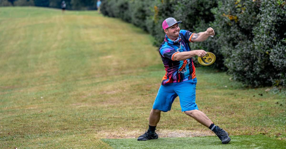 A man shows a lot of effort as he reaches back to throw a disc from the tee pad