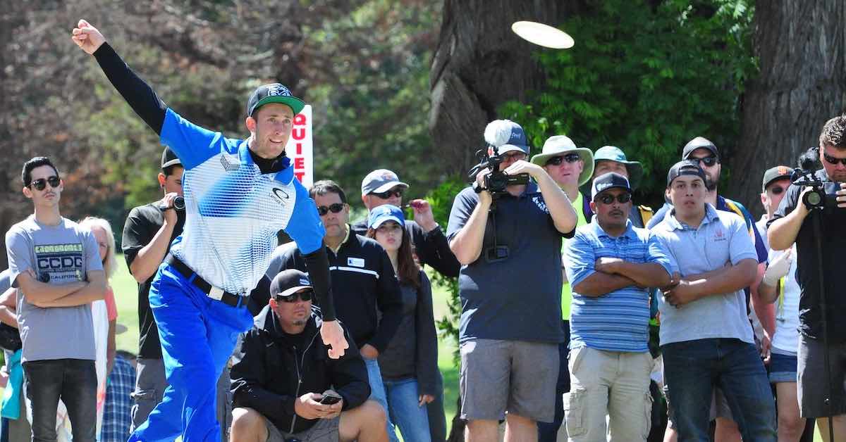 Pro disc golfer Ricky Wysocki, clad in blue and white, driving in front of a crowd