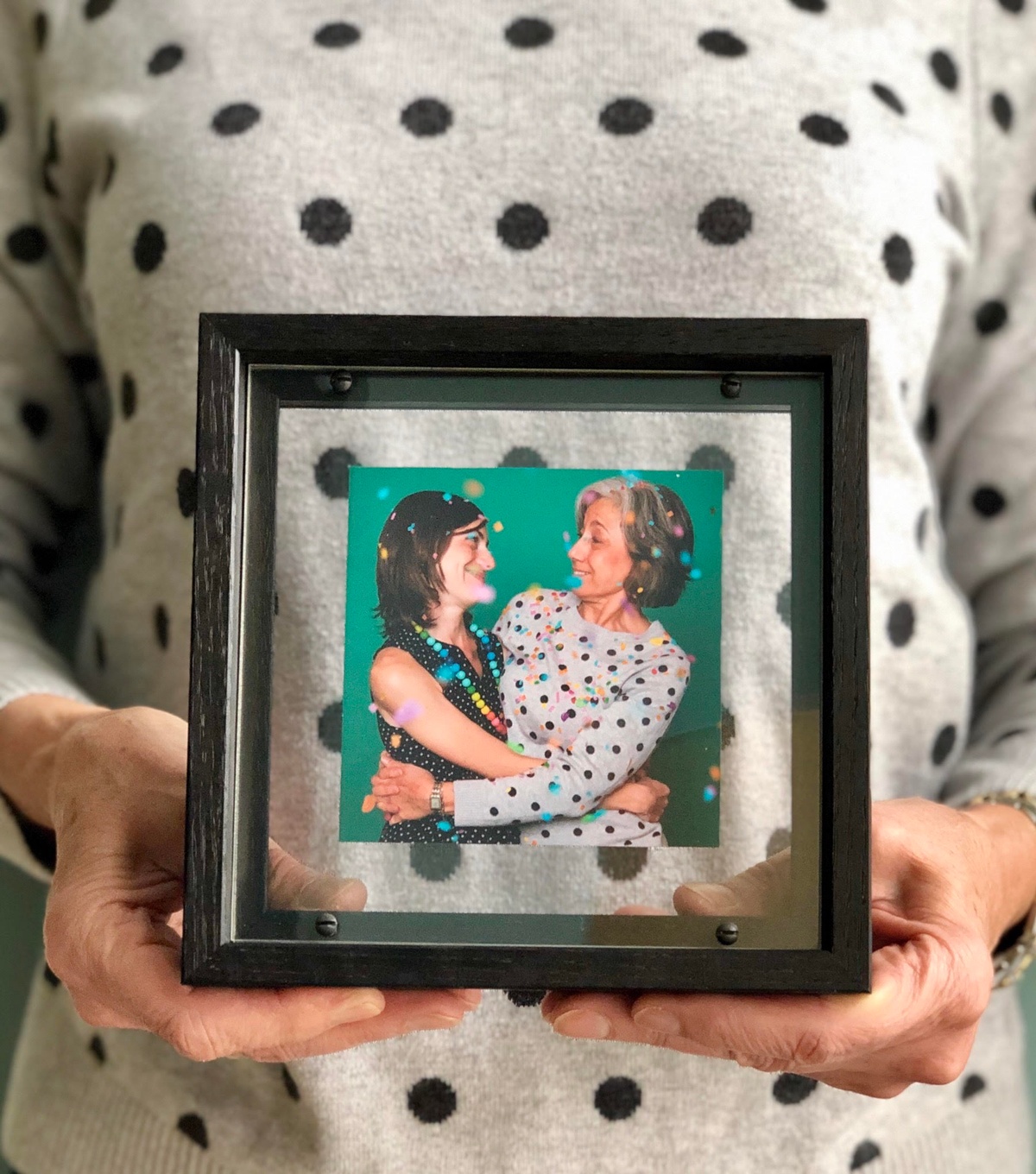 Small photo of two women being held by two hands in black frame