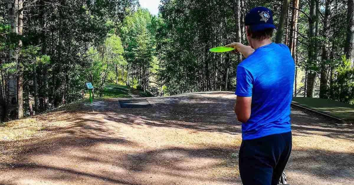 Young man in blue tee shirt lining up a disc golf shot