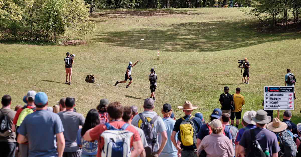 A crowd on watches someone throw a disc golf drive