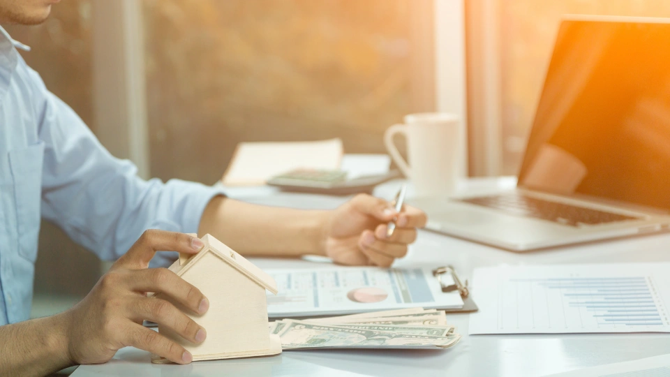 Person writing on a clipboard holding a small wooden home