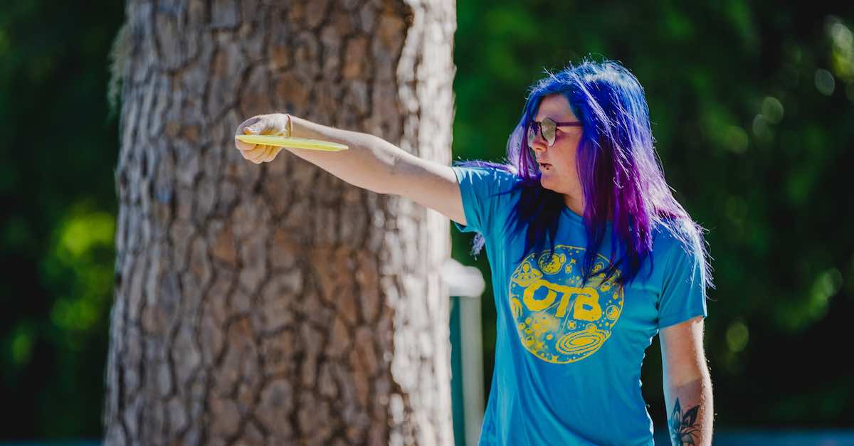Player with long purple and blue hair lines up disc golf drive