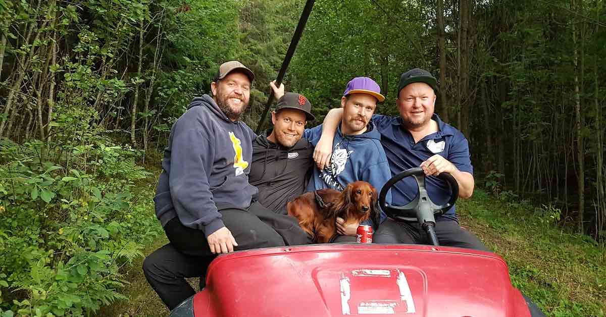 4 men on a golf card in hoodies and with baseball caps smiling for the camera
