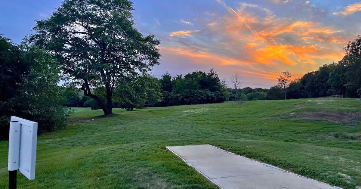 A concrete disc golf tee pad in a mown area with scattered trees