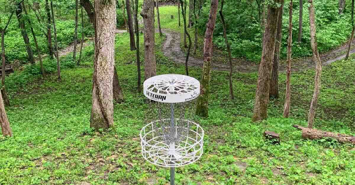 A disc golf basket in a wooded area on top of a slope