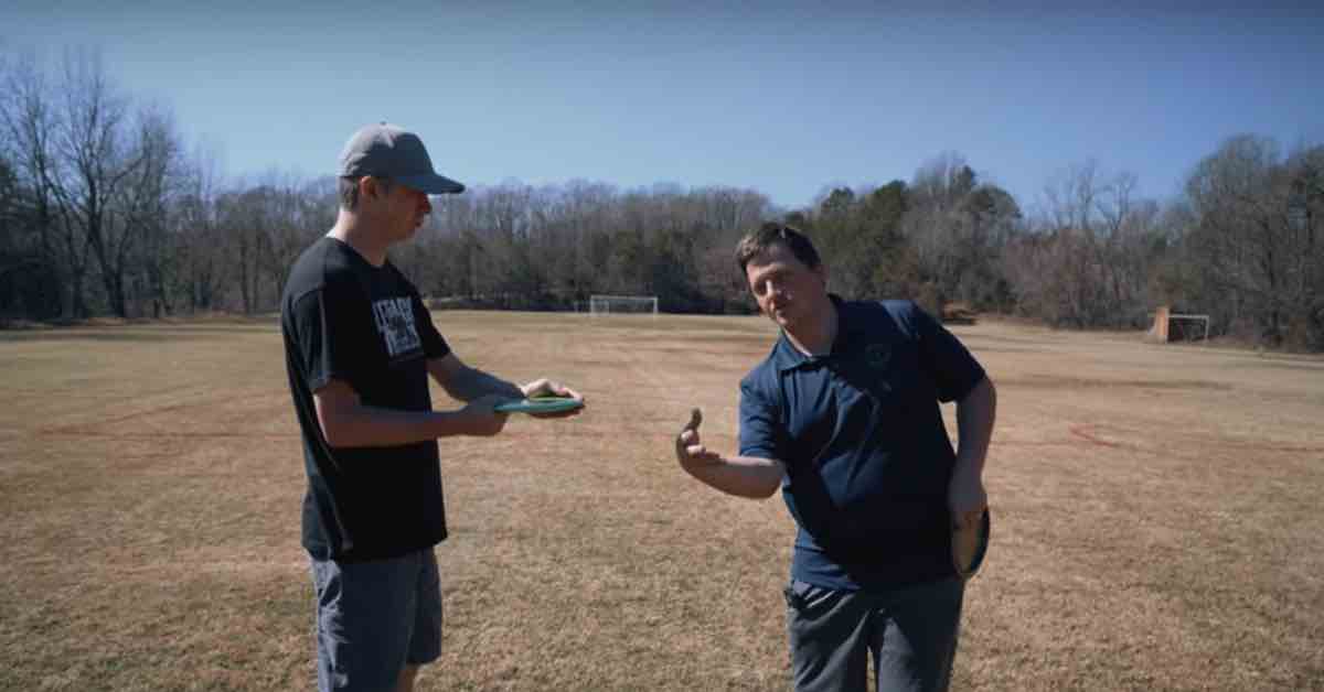 One man demonstrating disc glf forehand form to another