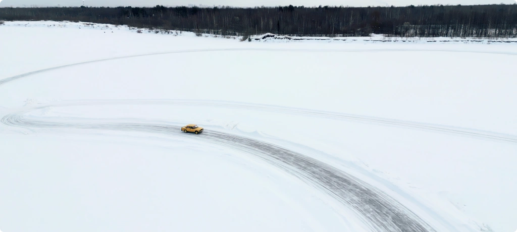 A yellow car seen from a distance traveling along a road in the middle of a snowy landscape