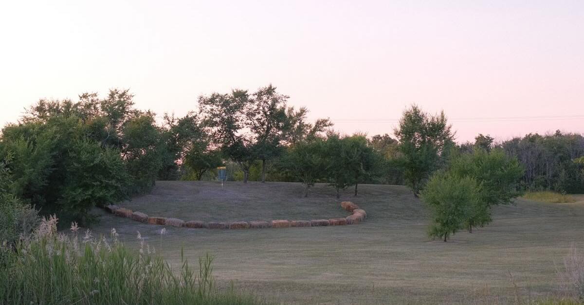 a semi-circle of hay bales creates an island green around a disc golf basket on a hillside