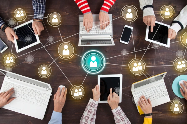 Six people sitting around a table with devices. They are interconnected by lines and icons of people.