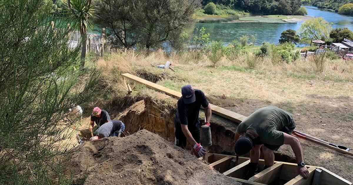 Men working to build a wooden staircase in a park with views of river behind