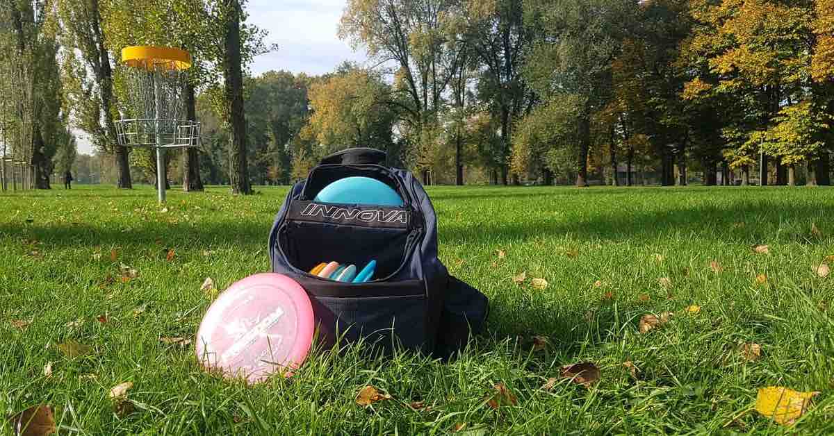 A disc golf basket and disc golf bag in a mowed park