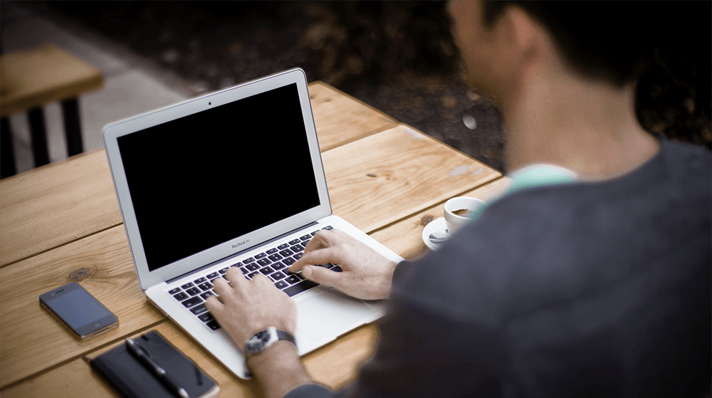 Man typing on laptop seated at park bench