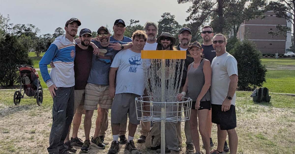 A group poses for a photo surrounding a disc golf basket