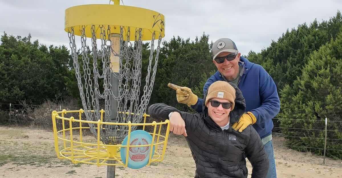 Two men posing next to a disc in a yellow disc golf basket