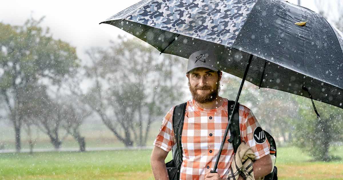 Chris Dickerson smiles into the camera while heavy rain falls on his black umbrella