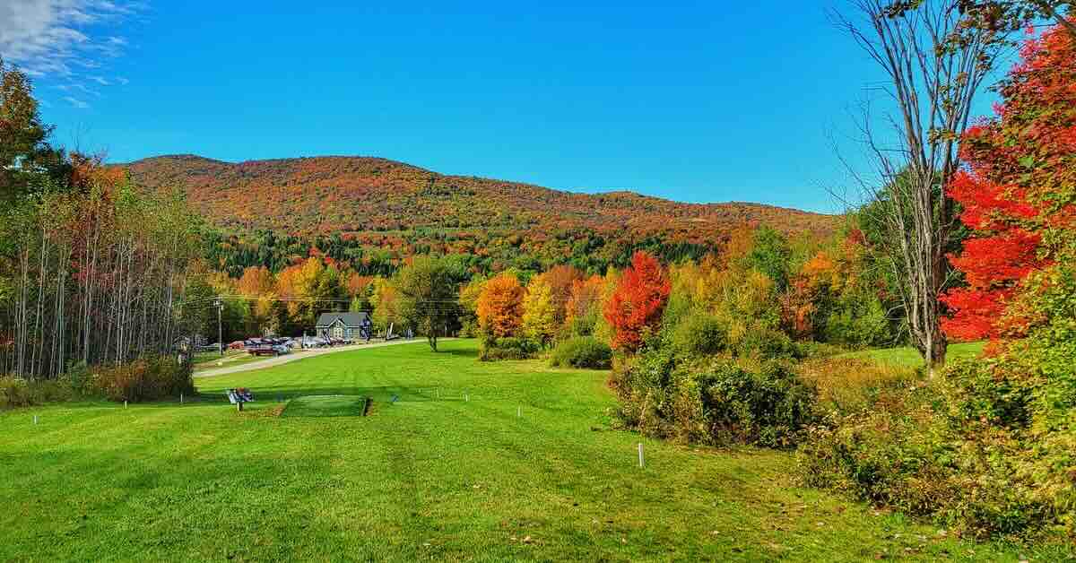 A mown disc golf fairway on top of a hill overlooks a fall landscape of tree-covered mountains