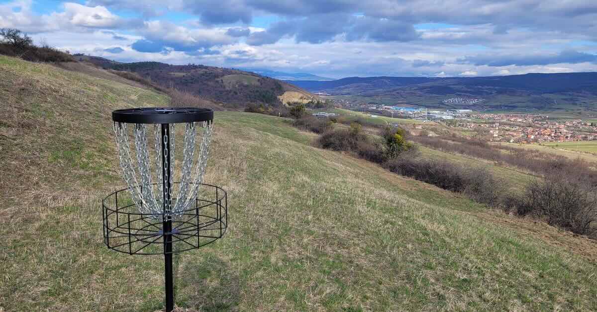 Black disc golf basket on a hillside with an expansive view in the distance