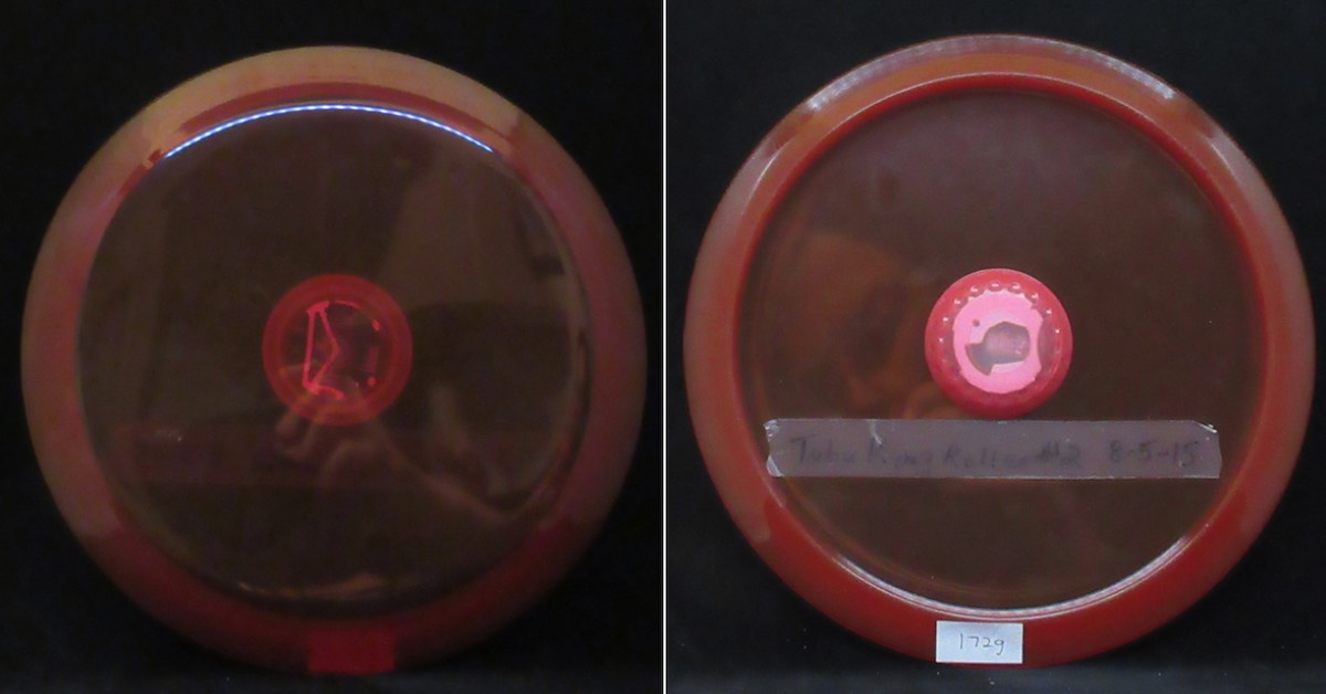 A pinkish orange tinted disc that is largely transparent. In its center is a small mechanical device covered by the disc's plastic