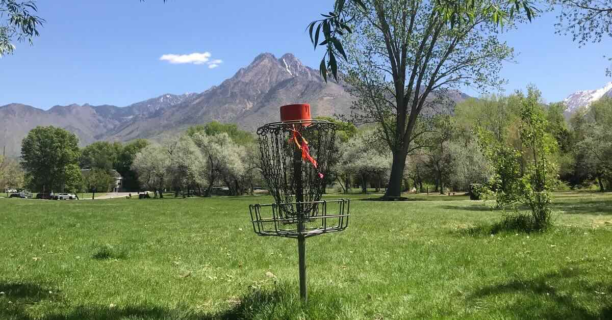 Older disc golf basket with red tape in it and a mountain in the background