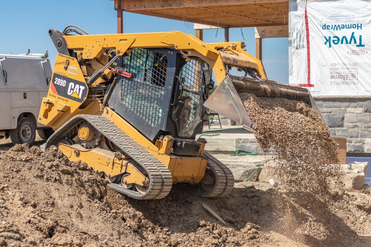 Yellow CAT compact track loader dumping dirt into a hole on a job site