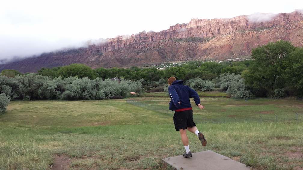 A man on a disc golf tee in front of a dramatic backdrop of red cliffs
