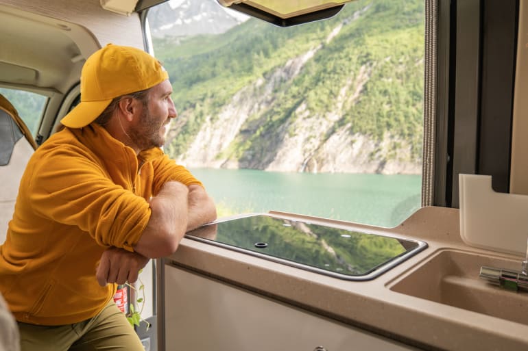 man looking at lake out of RV window