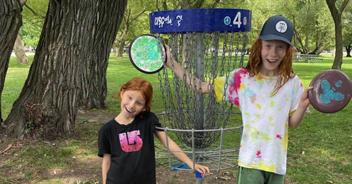 Two red-haired children near a disc golf basket in a park