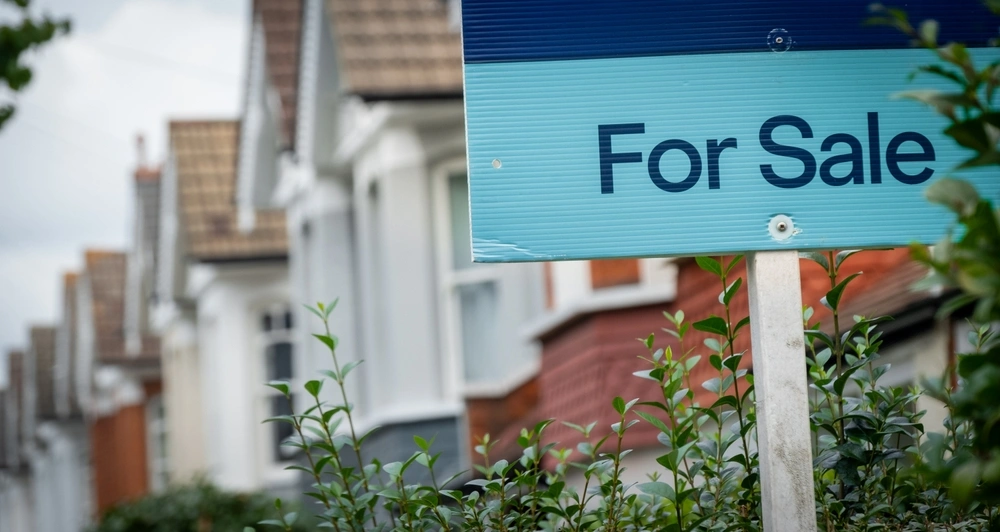 For sale sign with a row of houses behind