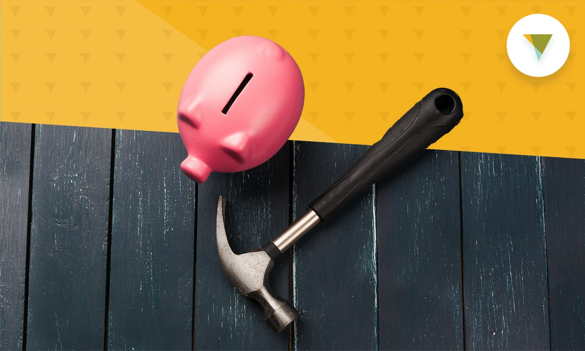 Piggy bank sitting next to a hammer on a table.