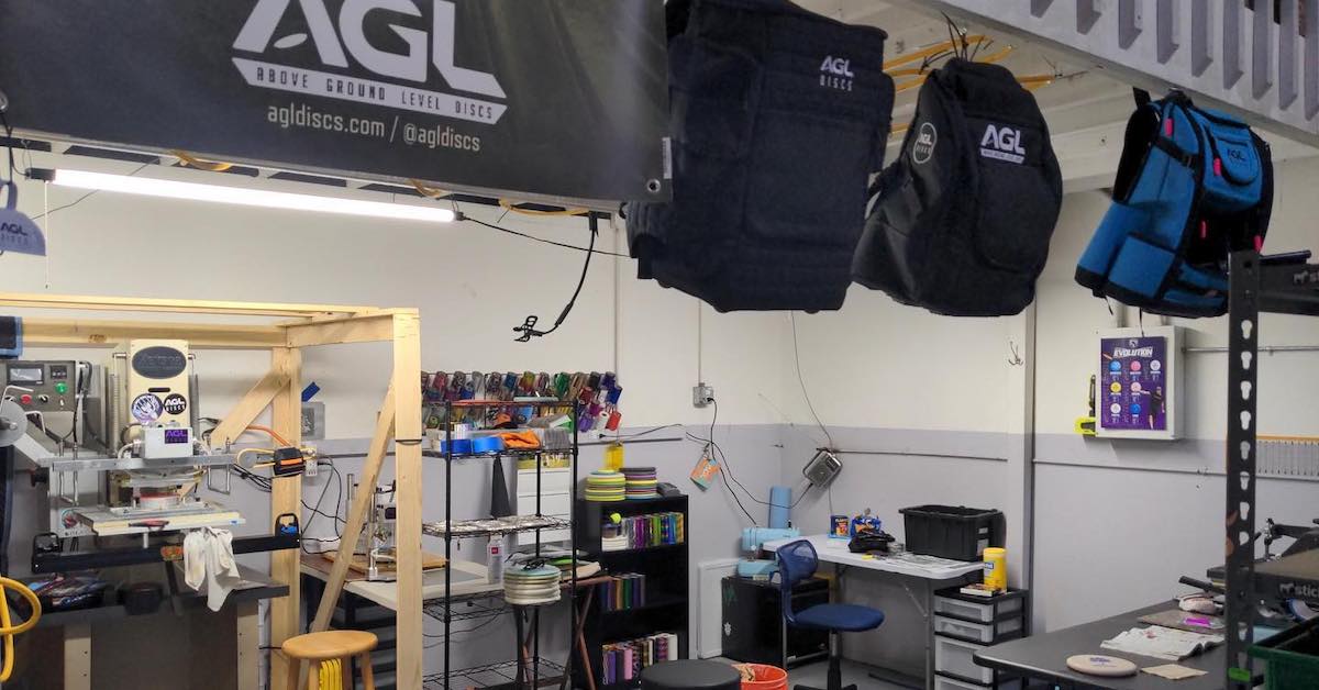 A bare-bones space withdisc printing, disc golf bags hanging, and disc-making equipment
