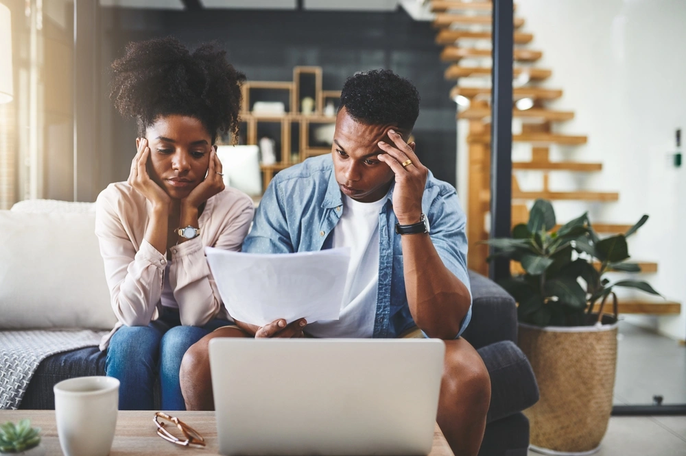 worried couple sat at a table looking at their laptop and paperwork