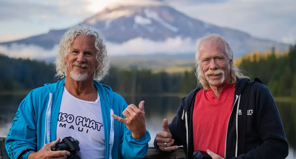 Two men pose for a photo in front of volcano.